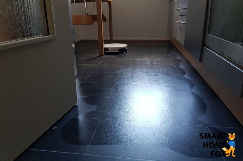 Man sieht den Yeedi Mop Roboter über den Boden fahren. Im Hintergrund steht die Ladestation.